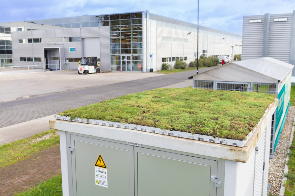 Groen dak op industrieel gebouw met elektrische installatie, moderne bedrijfspanden op de achtergrond