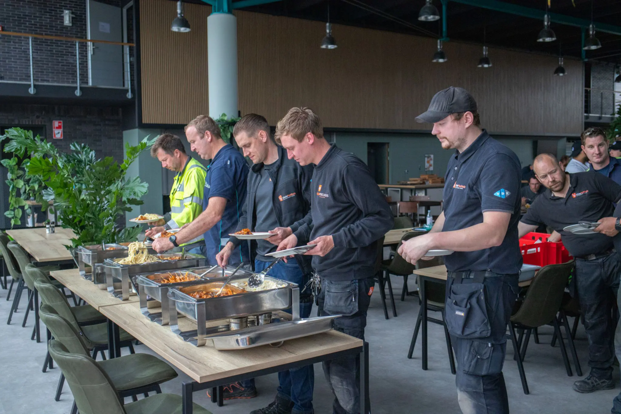 Werknemers in donkere uniformen serveren zichzelf eten uit chafing dishes tijdens een bedrijfslunch in moderne kantine