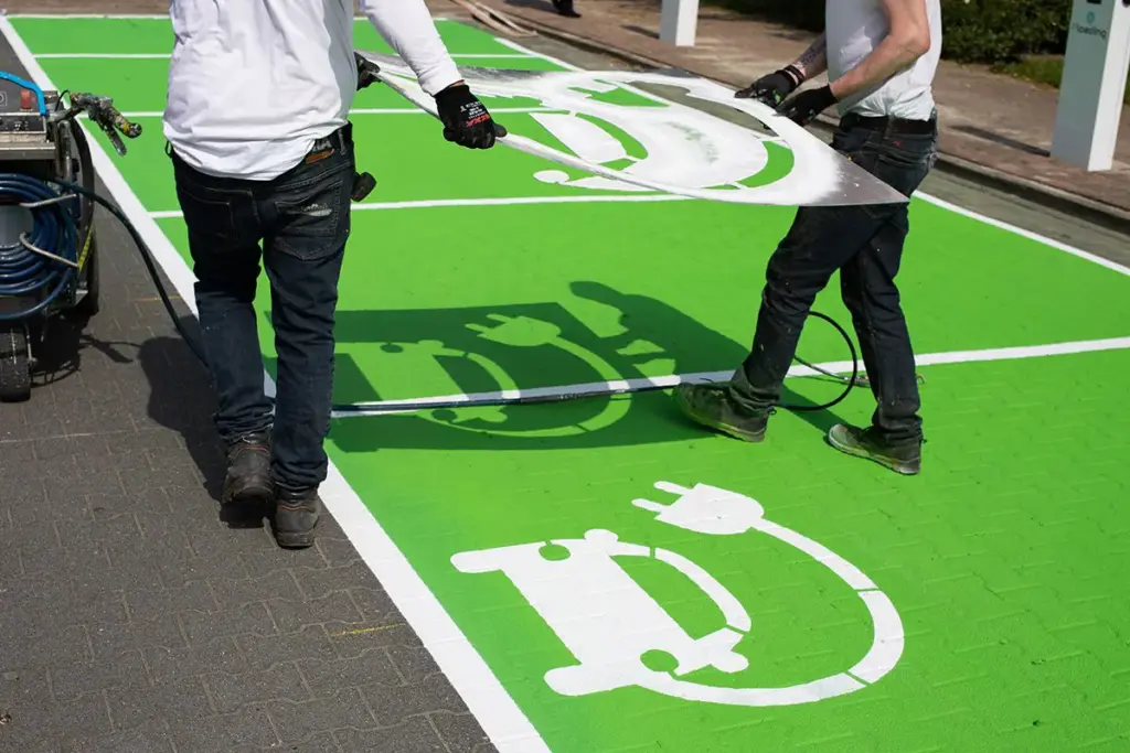 Werknemers installeren groene wegmarkering met elektrische auto oplaadsymbool voor EV-laadstation