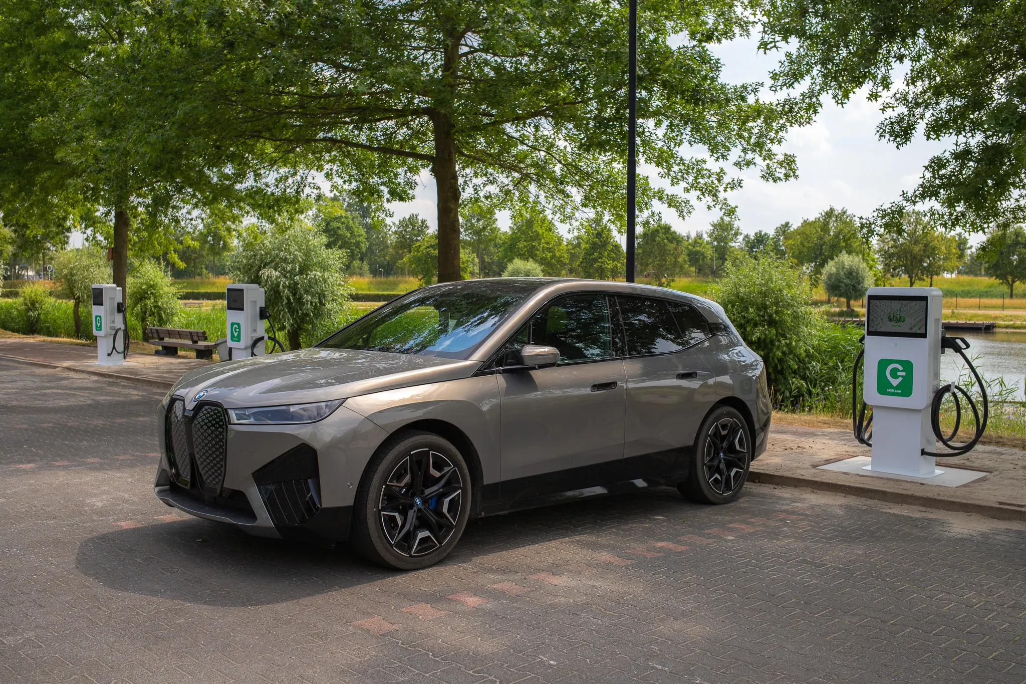BMW iX elektrische SUV aan DC laadpaal bij openbaar laadstation in groene omgeving