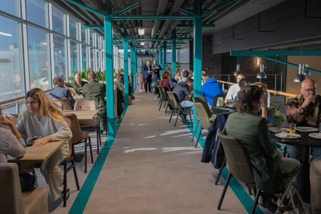 Moderne restaurant met turquoise structuur, grote ramen en gasten aan tafels in industriële setting