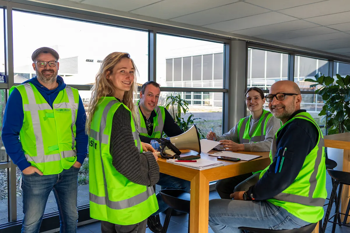 Team van vijf personen in groene veiligheidsvesten tijdens voorbereiding ontruimingsoefening