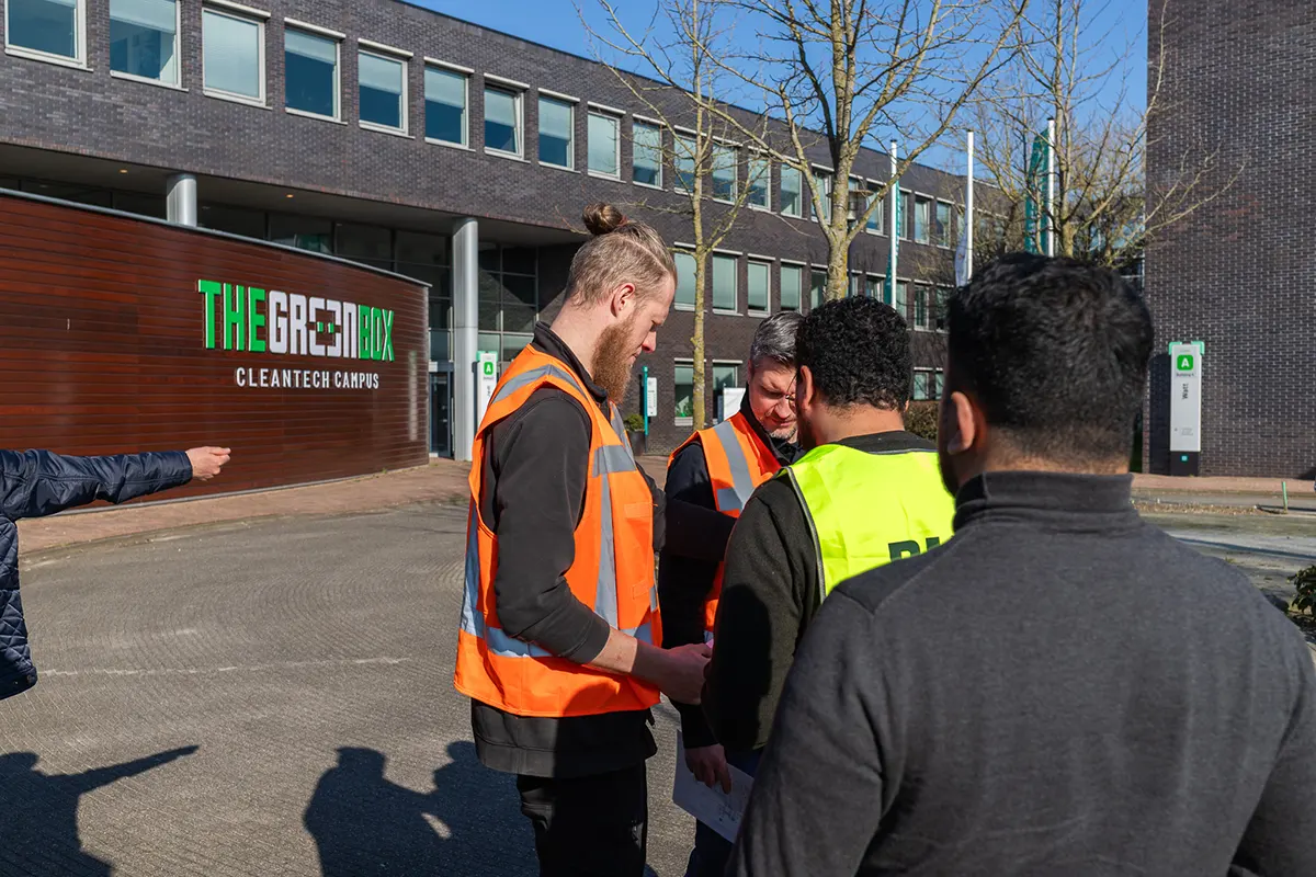 Groep mensen in veiligheidshesjes bij The Green Box Cleantech Campus gebouw tijdens ontruimingsoefening