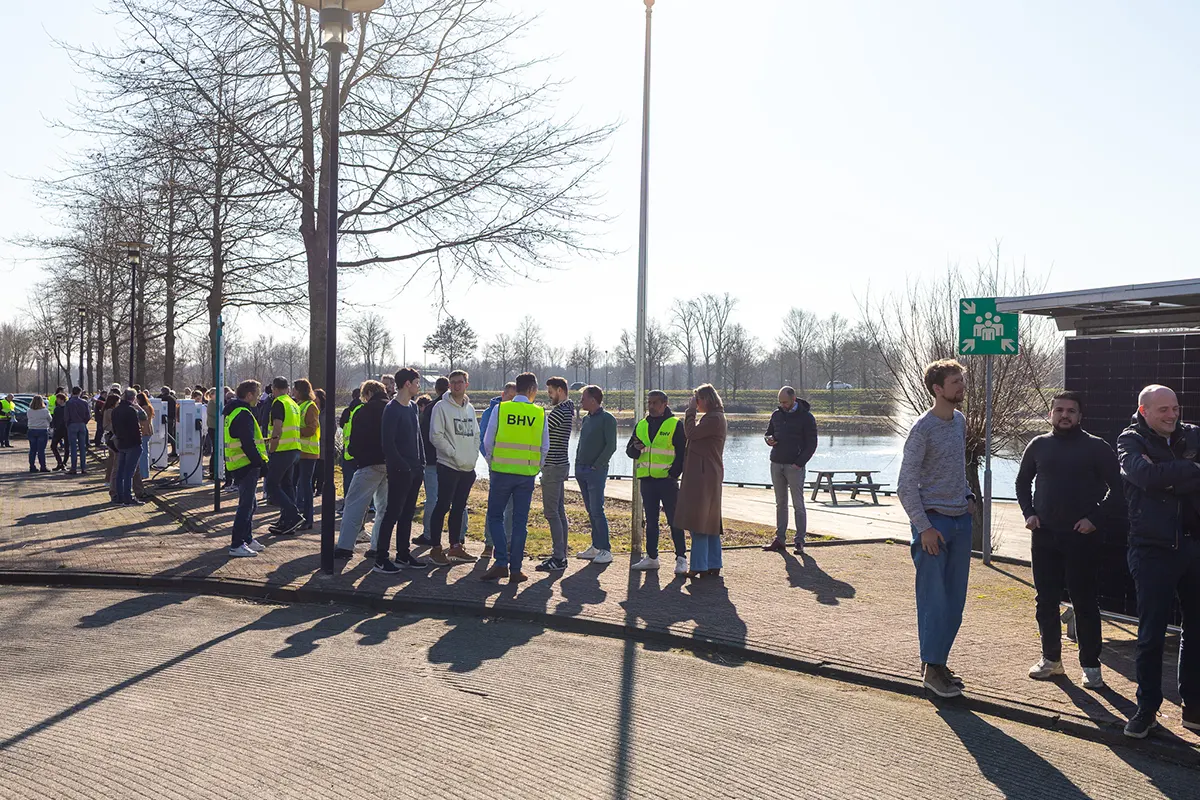 Groep mensen in veiligheidshesjes verzameld bij water, ontruimingsoefening The Green Box