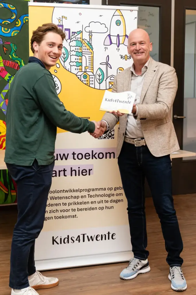 Twee mannen schudden handen bij Kids4Twente banner over technologie- en wetenschapsprogramma voor kinderen