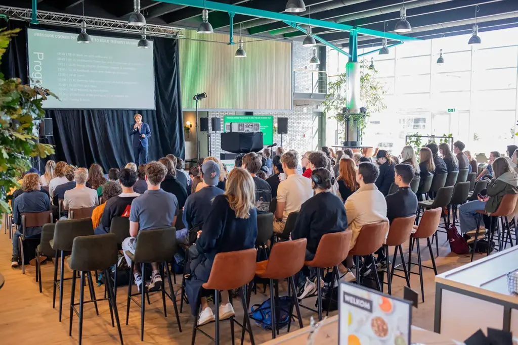 Spreker presenteert voor volle zaal tijdens tech-conferentie in moderne evenementenlocatie met industrieel design Cantonica The Green Box