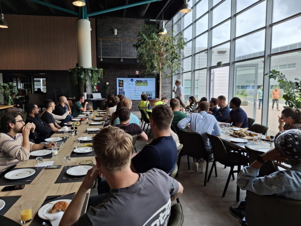 Groep mensen luistert naar presentatie in moderne vergaderruimte met grote ramen en planten tijdens zakelijke bijeenkomst