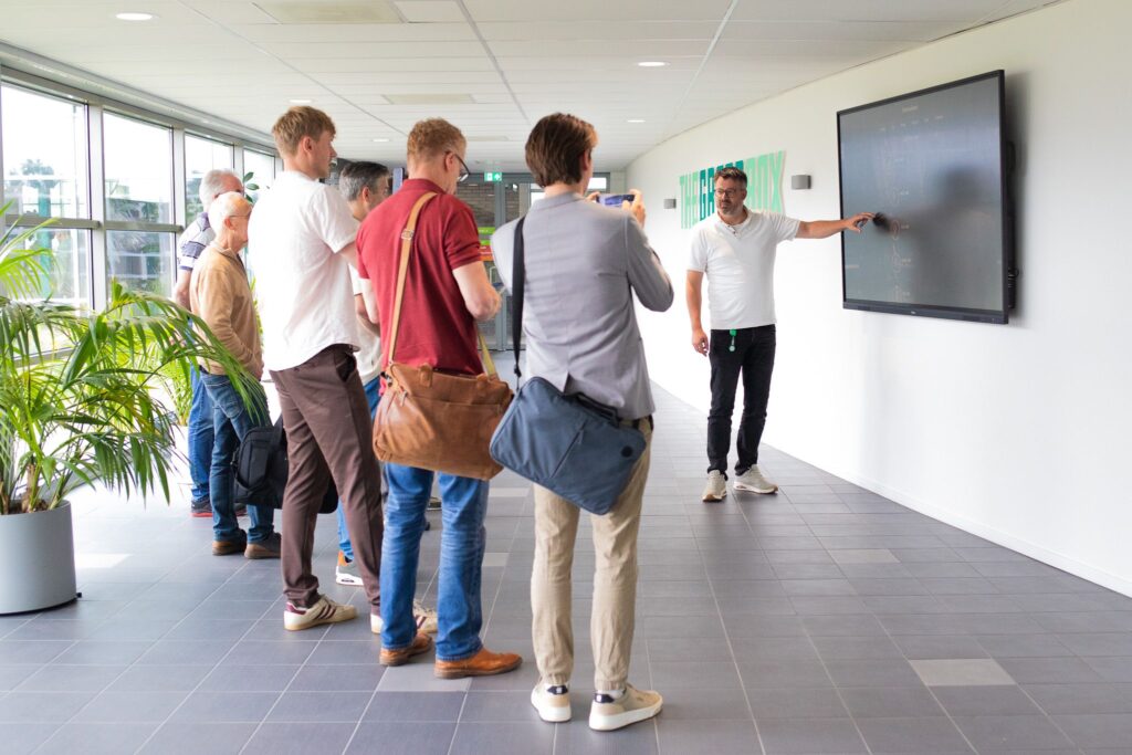 Groep professionals luistert naar presentatie bij interactief scherm in modern kantoor van The Greenbox.