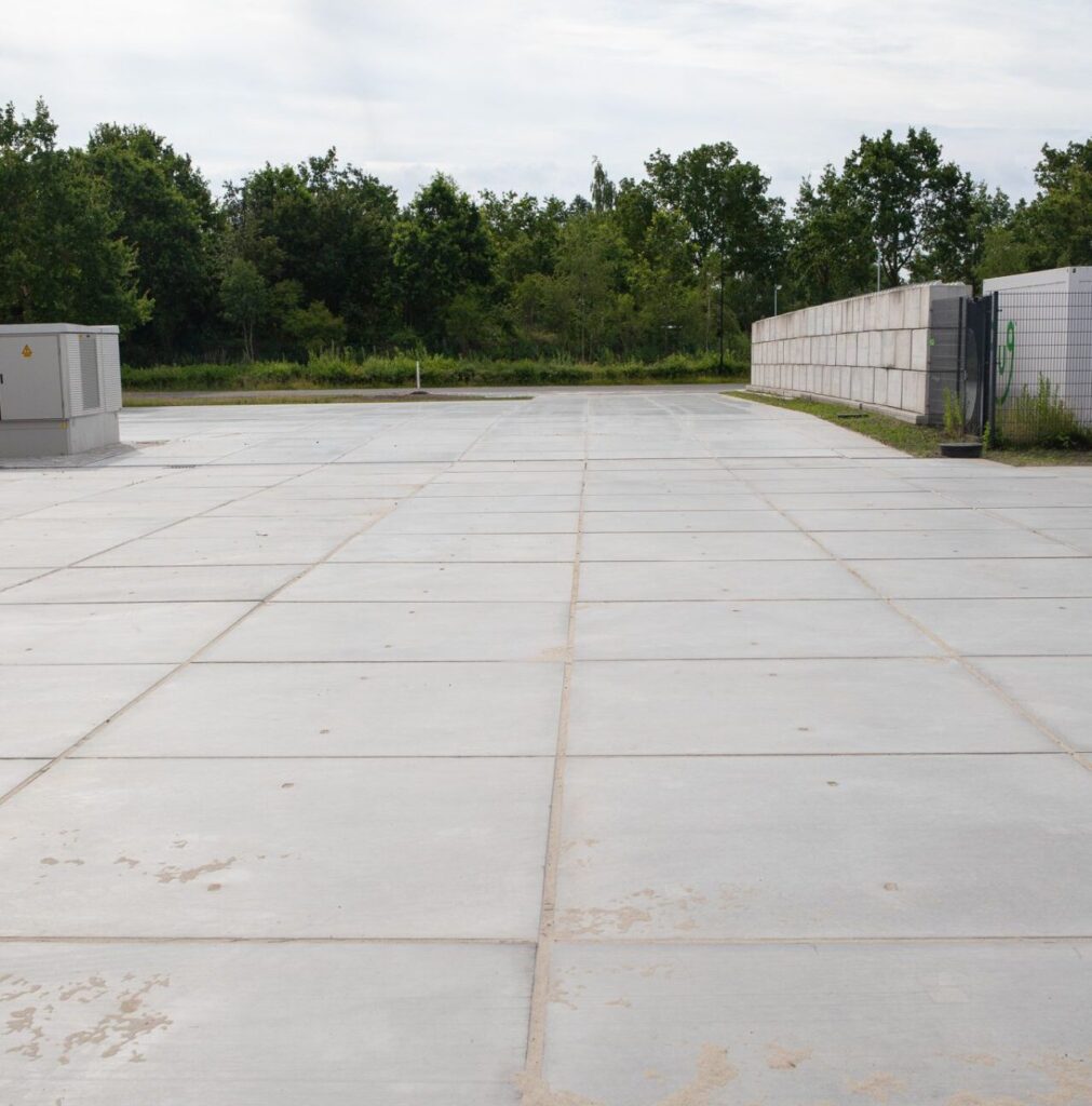 Lege betonnen buitenopslag met betonnen platen, omheining en groen op de achtergrond.