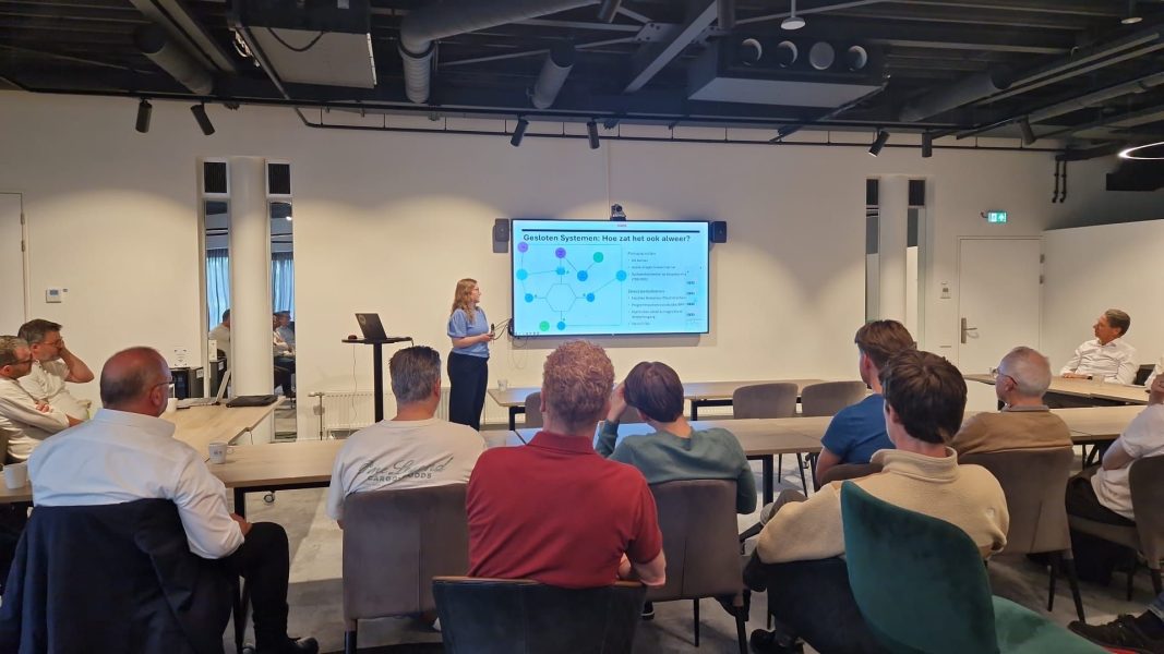 Presentatie over gesloten systemen in moderne vergaderzaal met spreker voor groot scherm en aandachtig publiek.